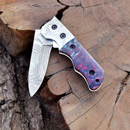 Compact outdoor Damascus steel folding pocket knife on tree log