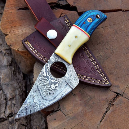 Hand-forged Damascus steel skinner knife – Pakka wood and bone handle – with leather sheath on tree stump.